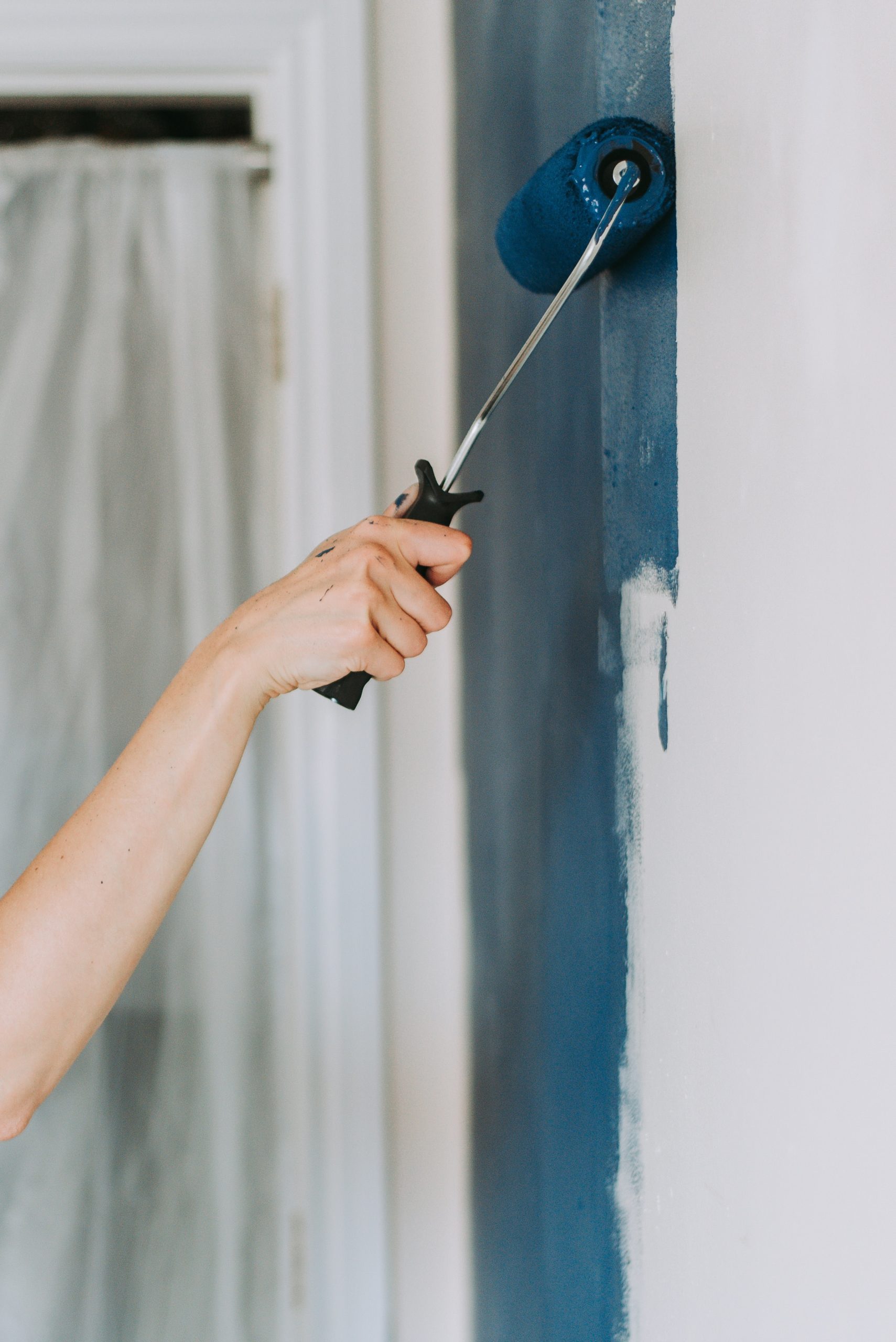 Peintre en tenue de travail appliquant de la peinture sur un mur, illustrant le savoir-faire en peinture d'intérieur